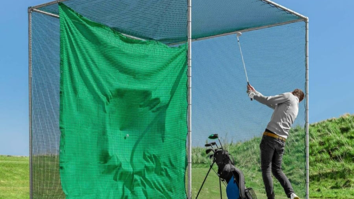 Golfer hitting a driver inside a heavy-duty garden golf cage with net and hitting mat set