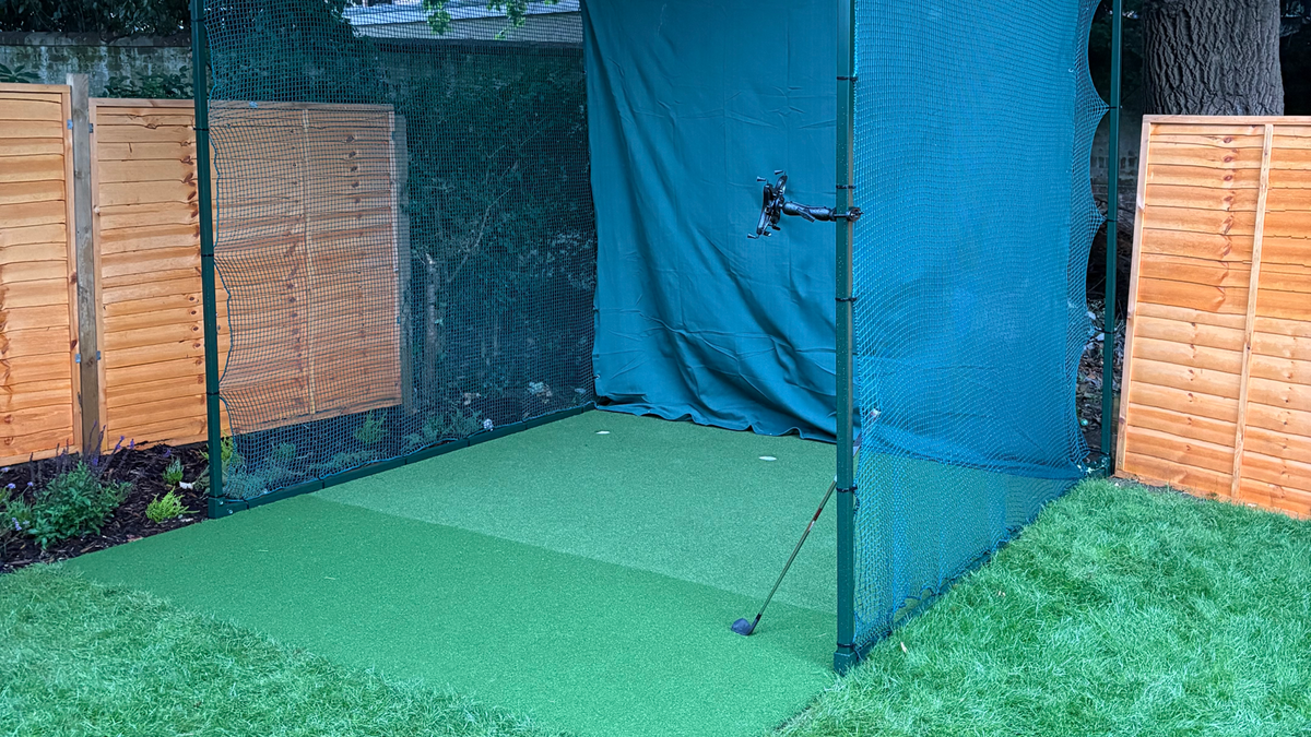 Garden golf practice cage with putting turf, backstop screen and launch monitor mount, iron lying ready on the mat — featured image