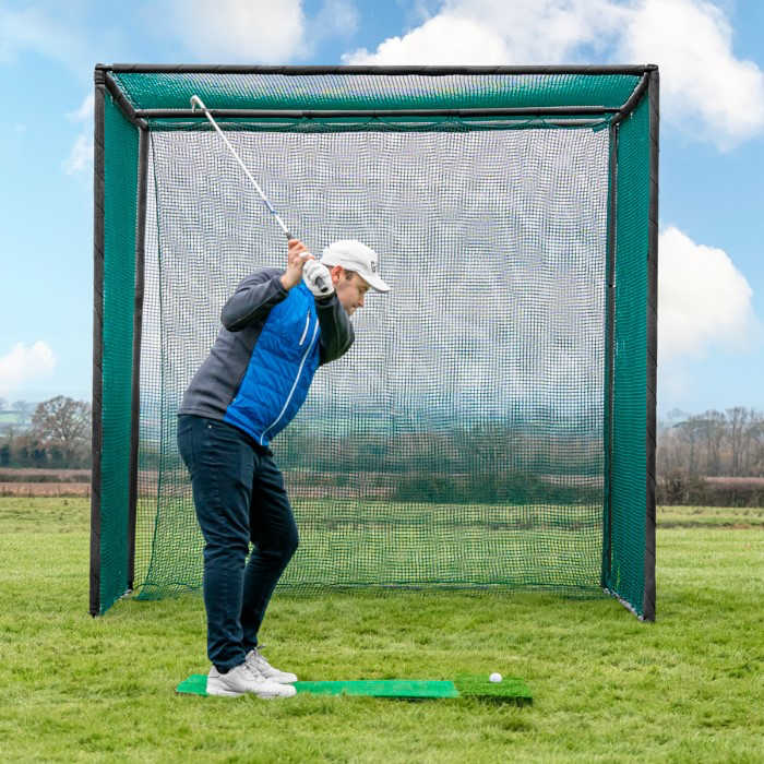 Golfer hitting driver inside a freestanding steel golf practice cage on a hitting mat