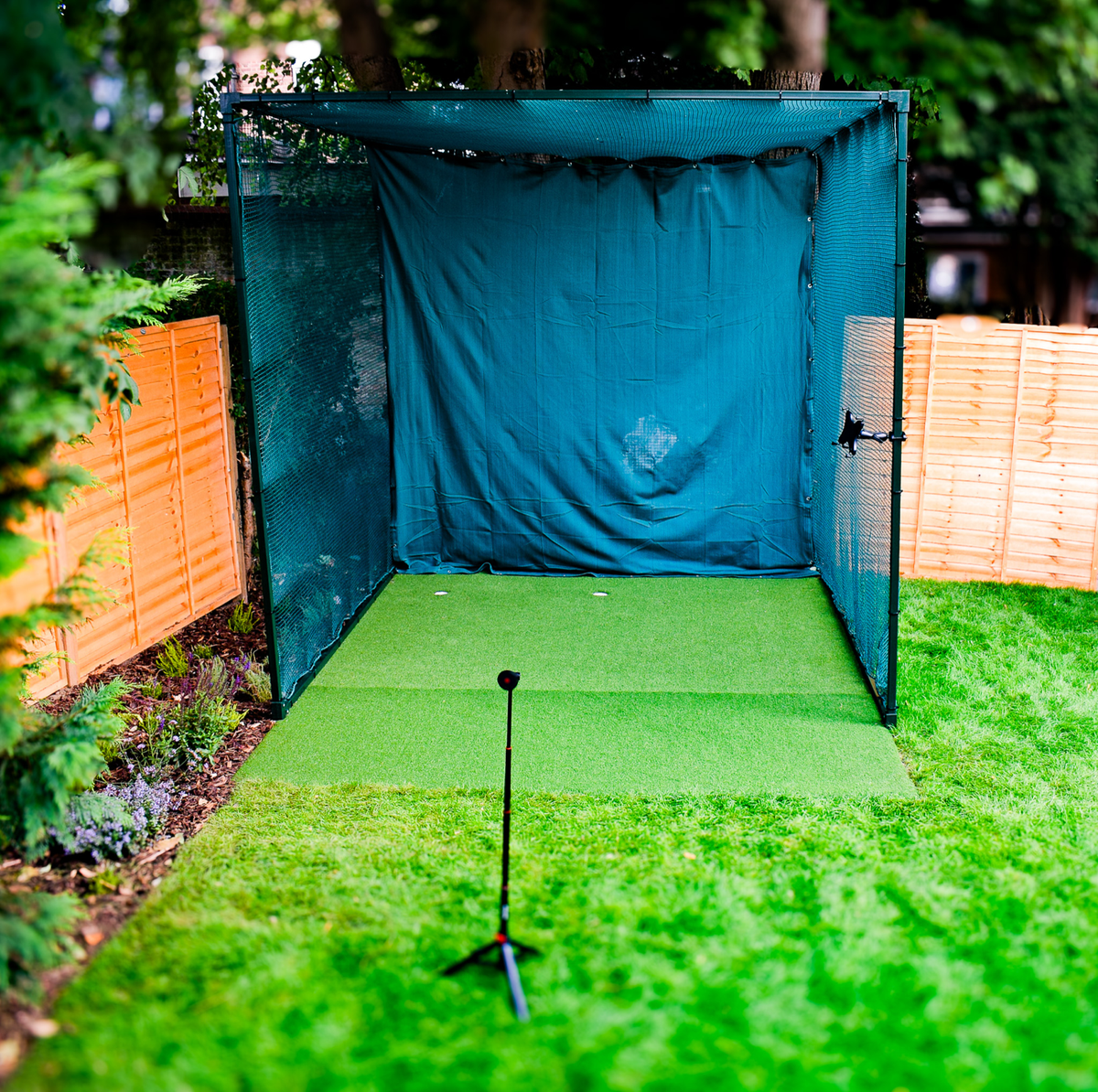 Garden golf cage practice station with hitting mat and launch monitor on a tripod