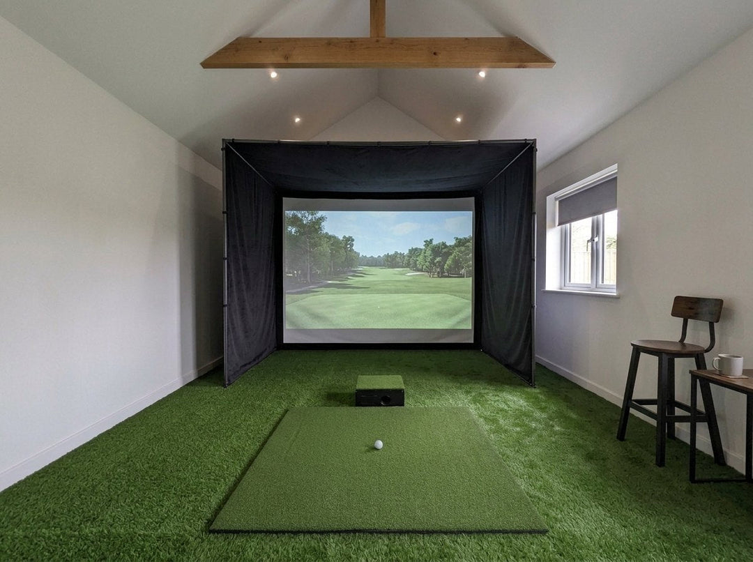 Illustration: golf simulator enclosure, hitting mat and a floor projector case in front of the mat in a UK converted outbuilding with a vaulted ceiling, daylight; artificial grass flooring
