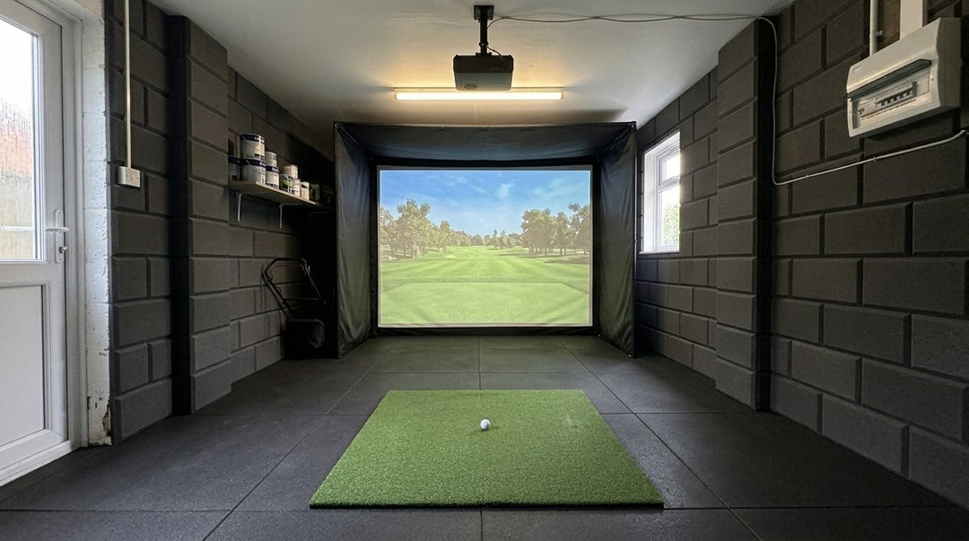 Illustration: golf simulator enclosure, hitting mat and a ceiling-mounted projector in a UK single garage, daylight; black rubber flooring and black foam wall tiles