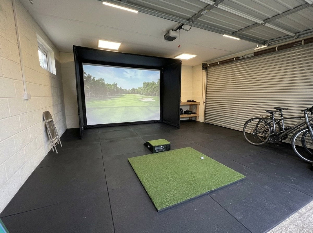 Illustration: golf simulator enclosure, hitting mat and a floor projector case in front of the mat in a UK double garage, daylight; black rubber flooring