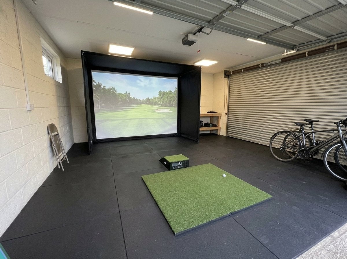 Illustration: golf simulator enclosure, hitting mat and a floor projector case in front of the mat in a UK double garage, daylight; black rubber flooring