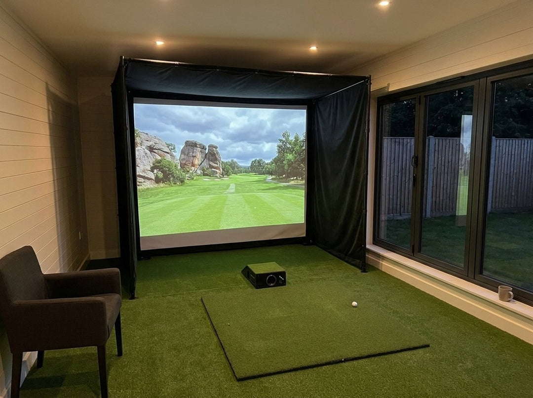 Illustration: golf simulator enclosure, hitting mat and a floor projector case in front of the mat in a UK garden room, evening light; artificial grass flooring