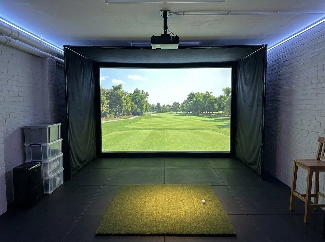 Illustration: golf simulator enclosure, hitting mat and a ceiling-mounted projector in a UK basement room, LED strip lighting; black rubber flooring
