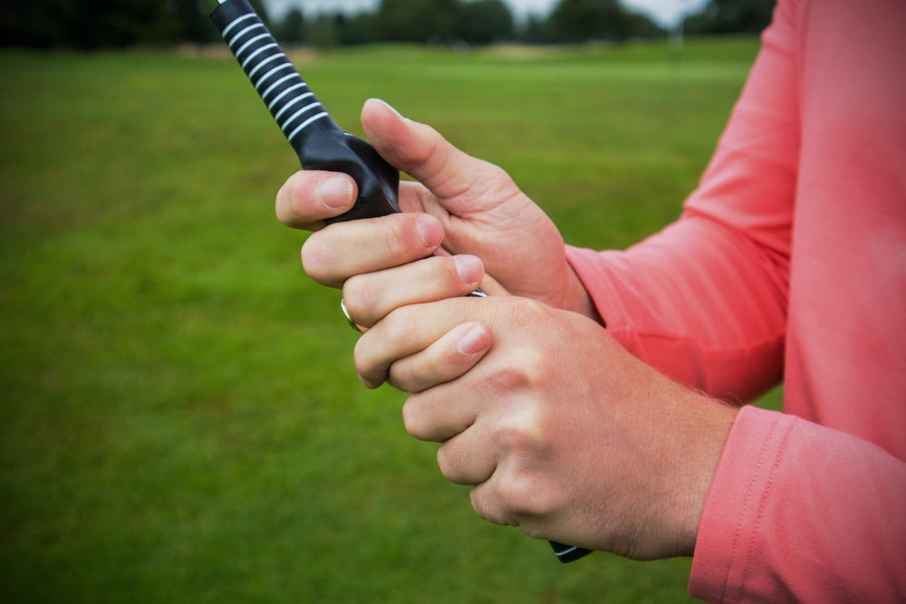 PGA TOUR Swing Weight and Training Grip Club next to a golf driving net for home practice